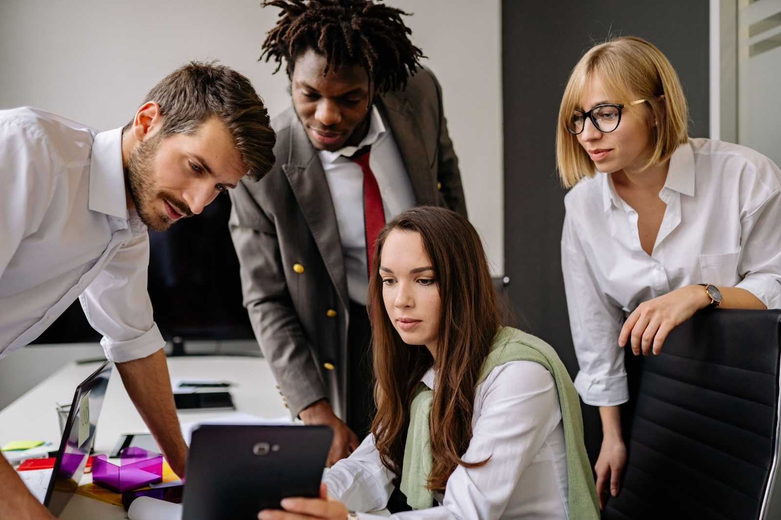 Four colleagues reviewing information together on a tablet in an office.