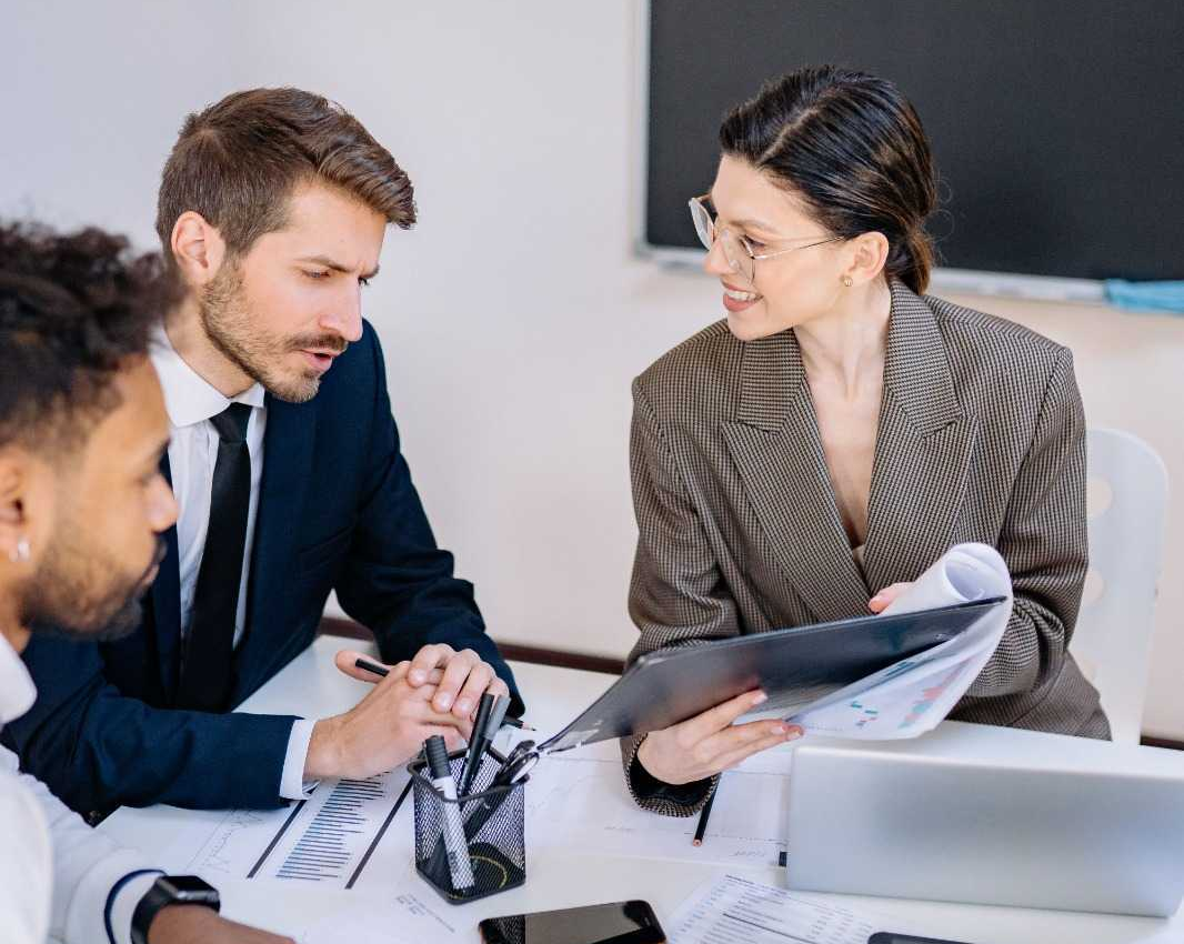 Professionals discussing a folder of reports around a meeting table.