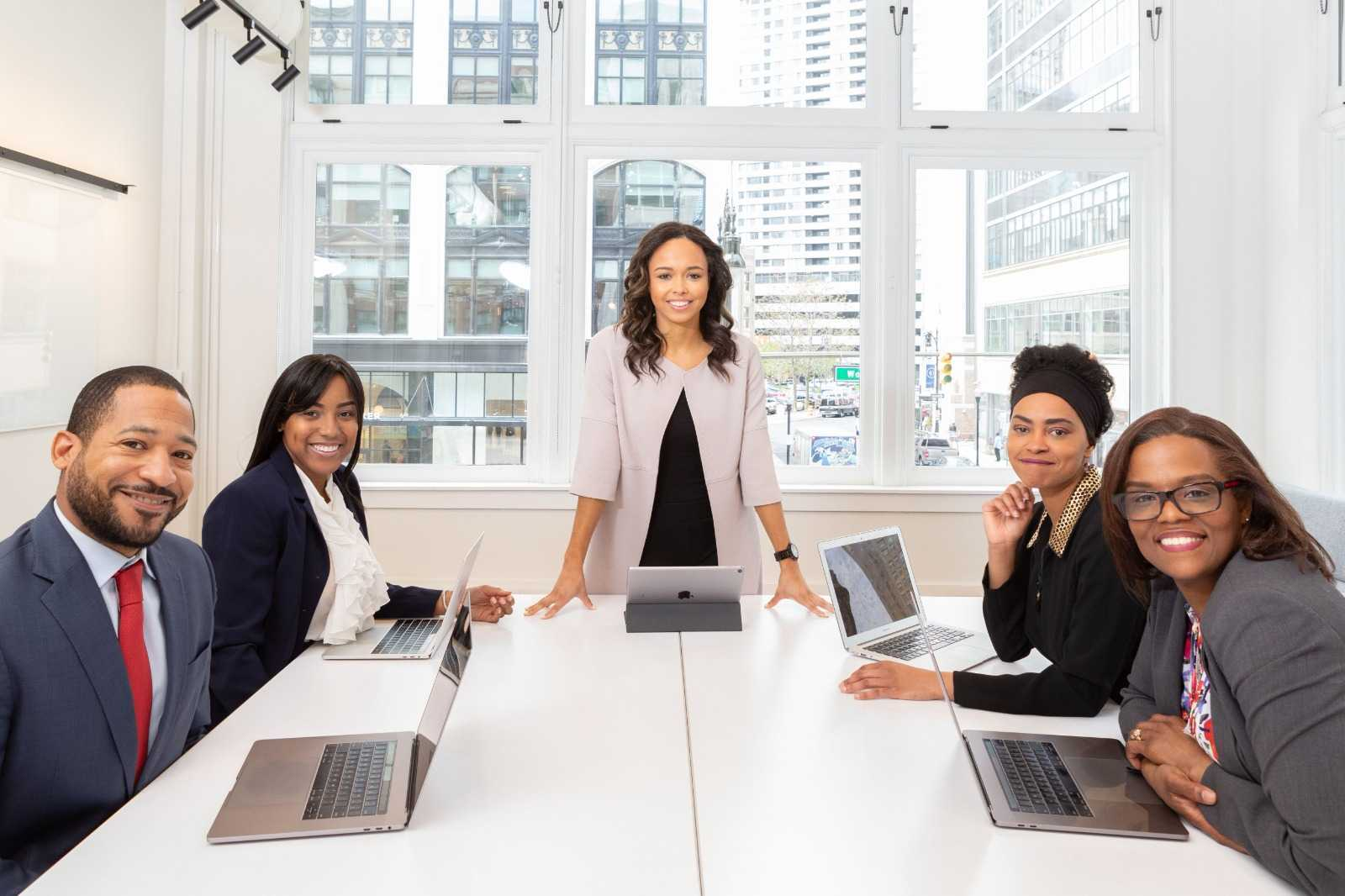 Five professionals gathered around a meeting table in a bright, window-lit office.